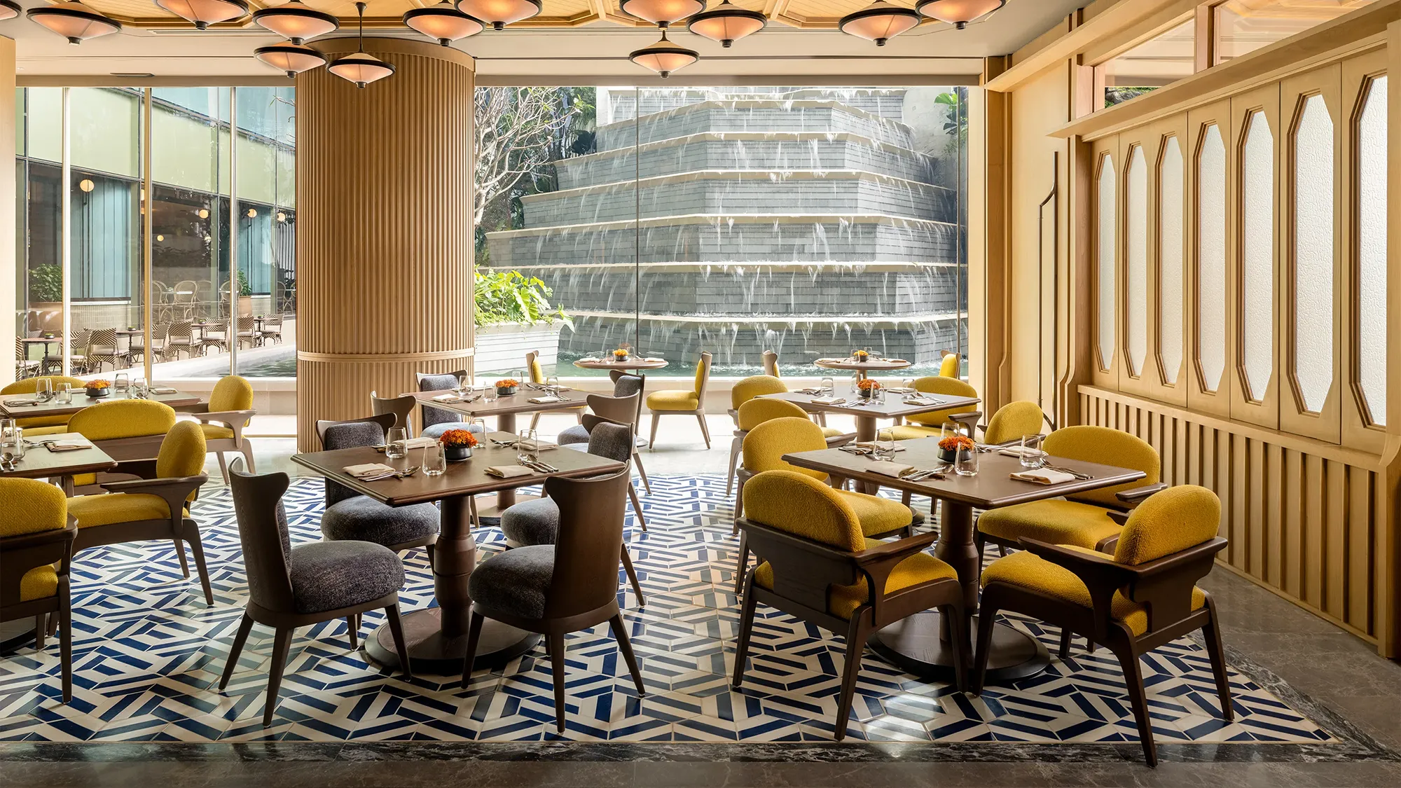 A manmade stepped waterfall outside of a window behind an indoor dining area set with rows of tables and chairs set for service