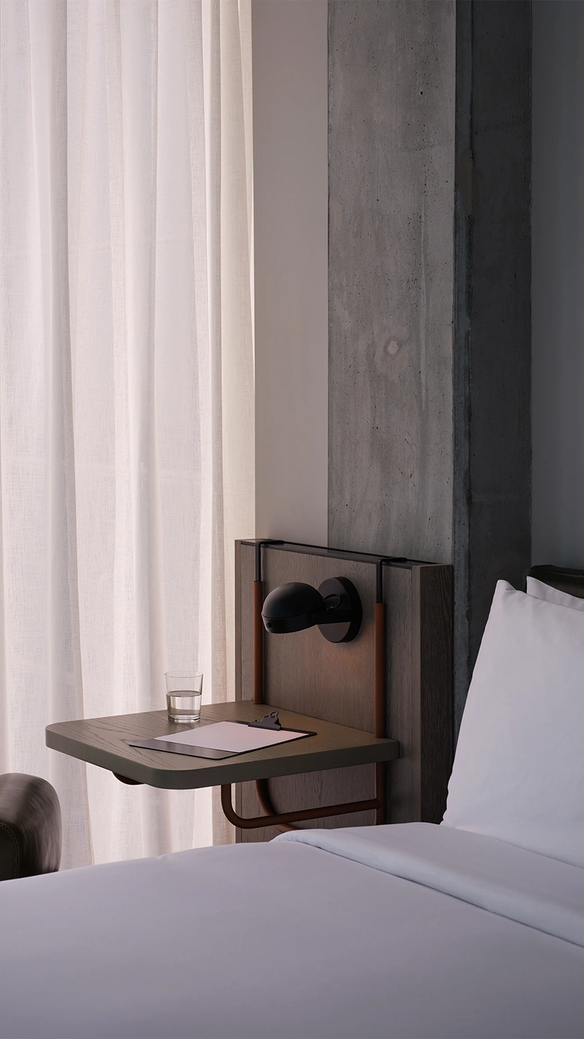 A wooden bedside table built into the wall with a light, papers, and a glass of water