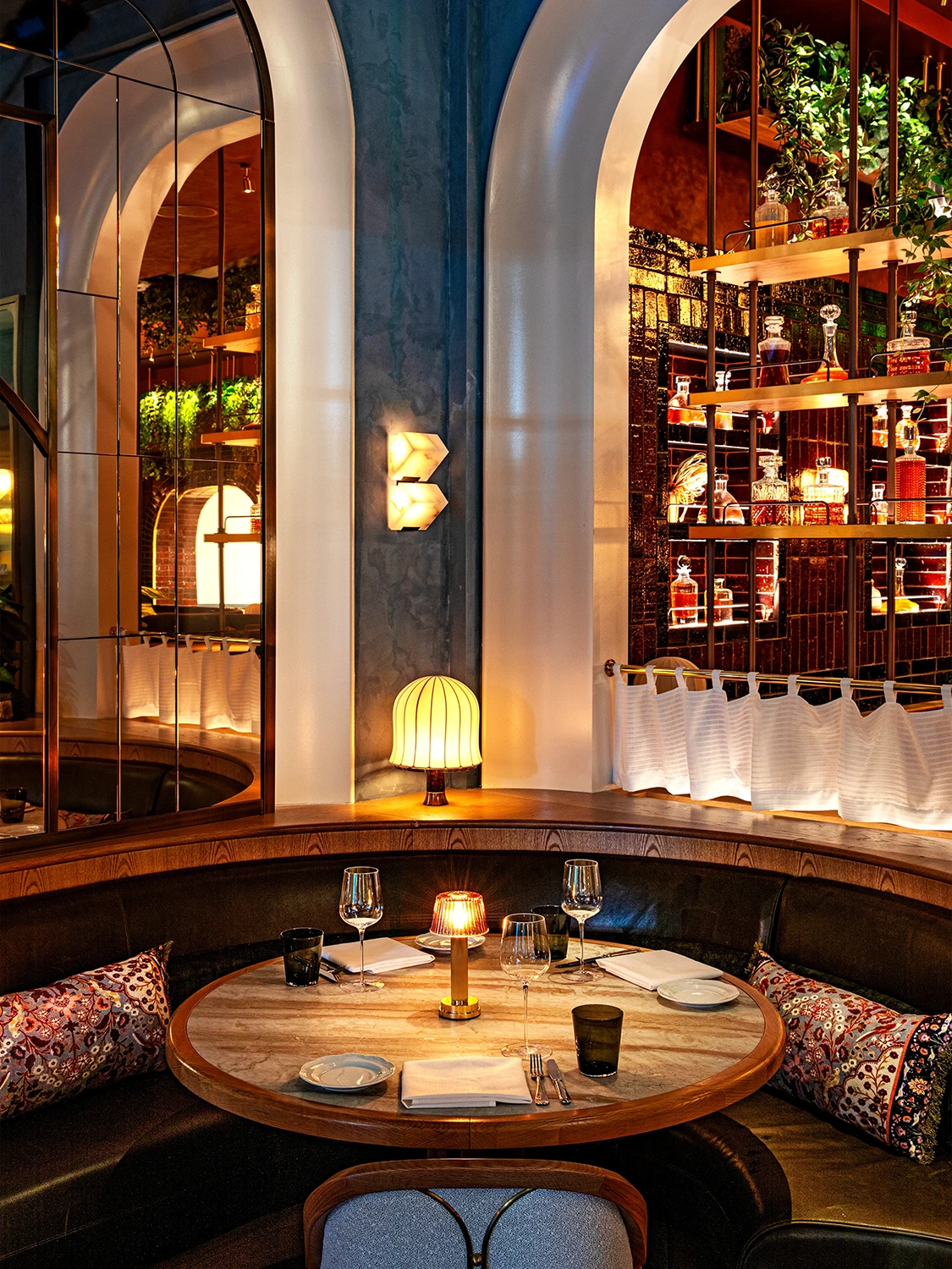 A cozy half-circle wooden booth in the corner of Bourbon Steakhouse restaurant behind a circular wooden table set for drinks and service