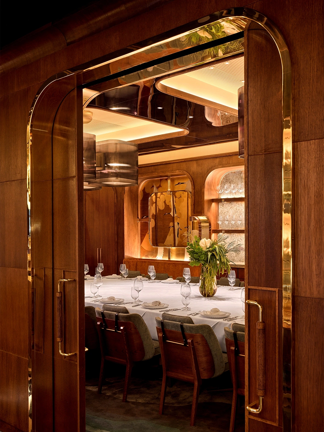 an arched wooden doorway looking into a white table cloth private dining area set with plates, glasses, and napkins