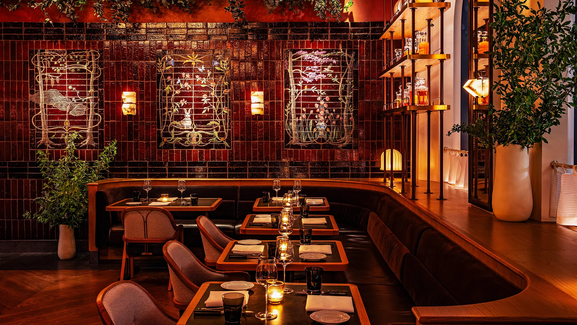 Line of set tables at Bourbon Steakhouse with lit candles in front of a red tile wall