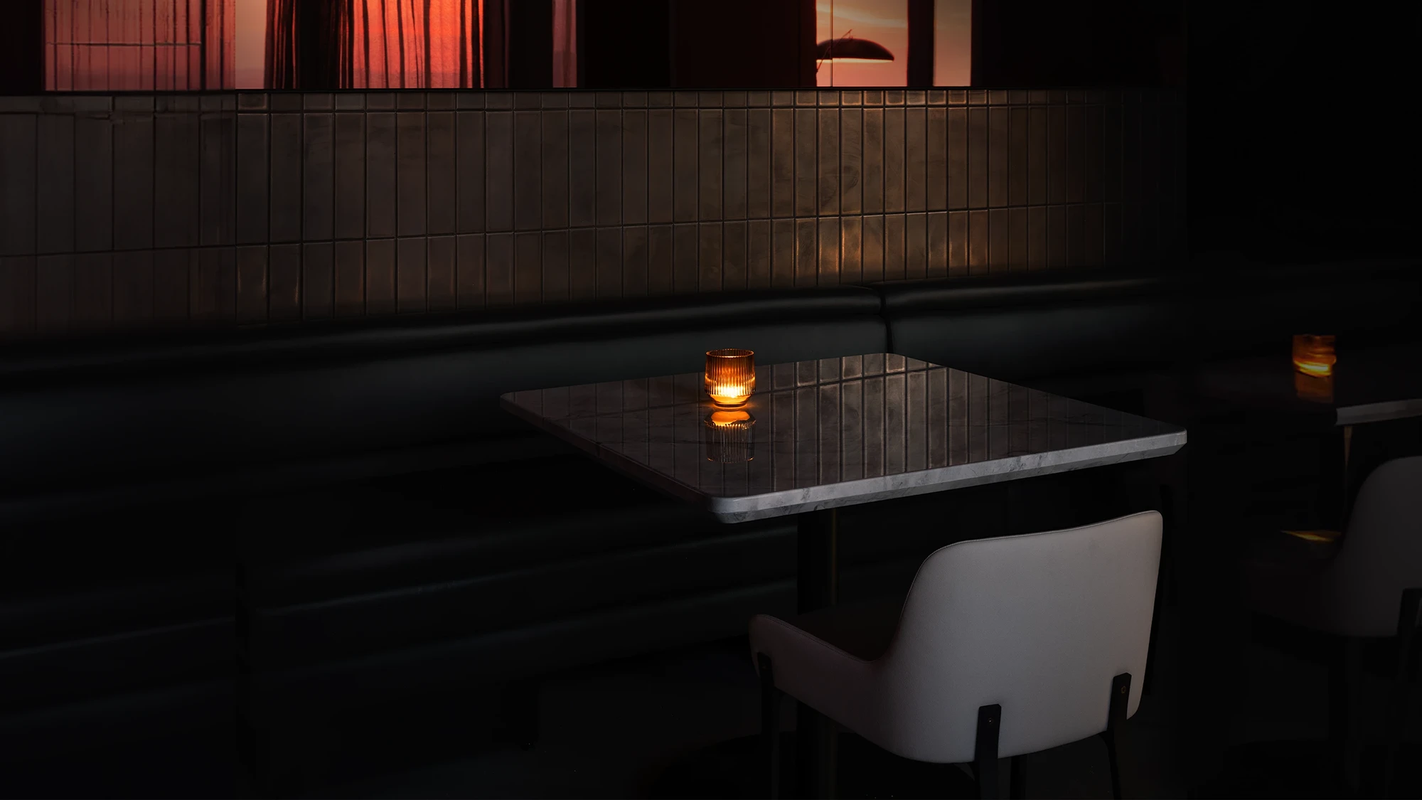 Moody lounge restaurant setting featuring a booth, a square table with a small light, and a beautifully designed chair.