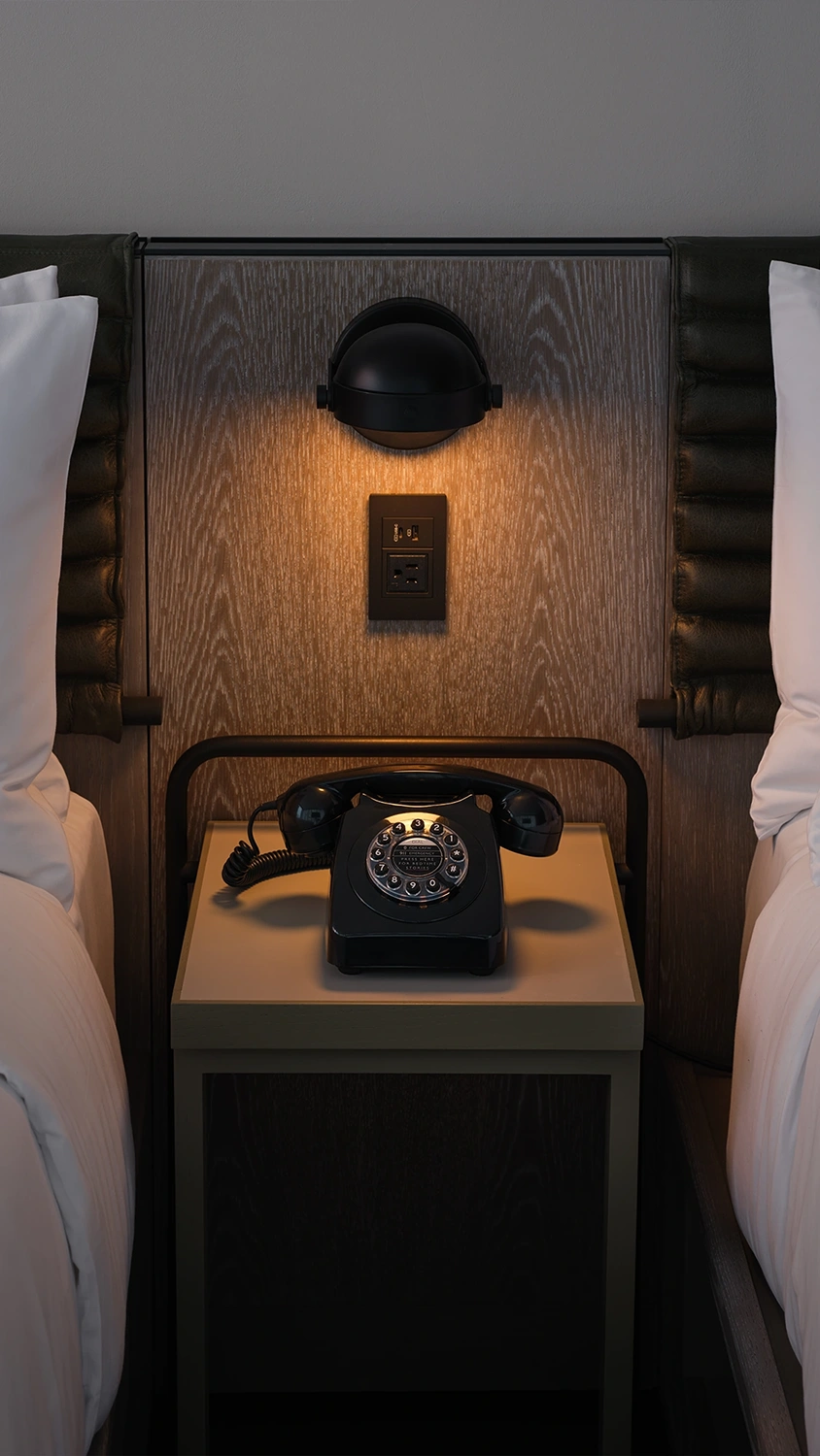 A hotel room bedside table with a classic wheel dial telephone