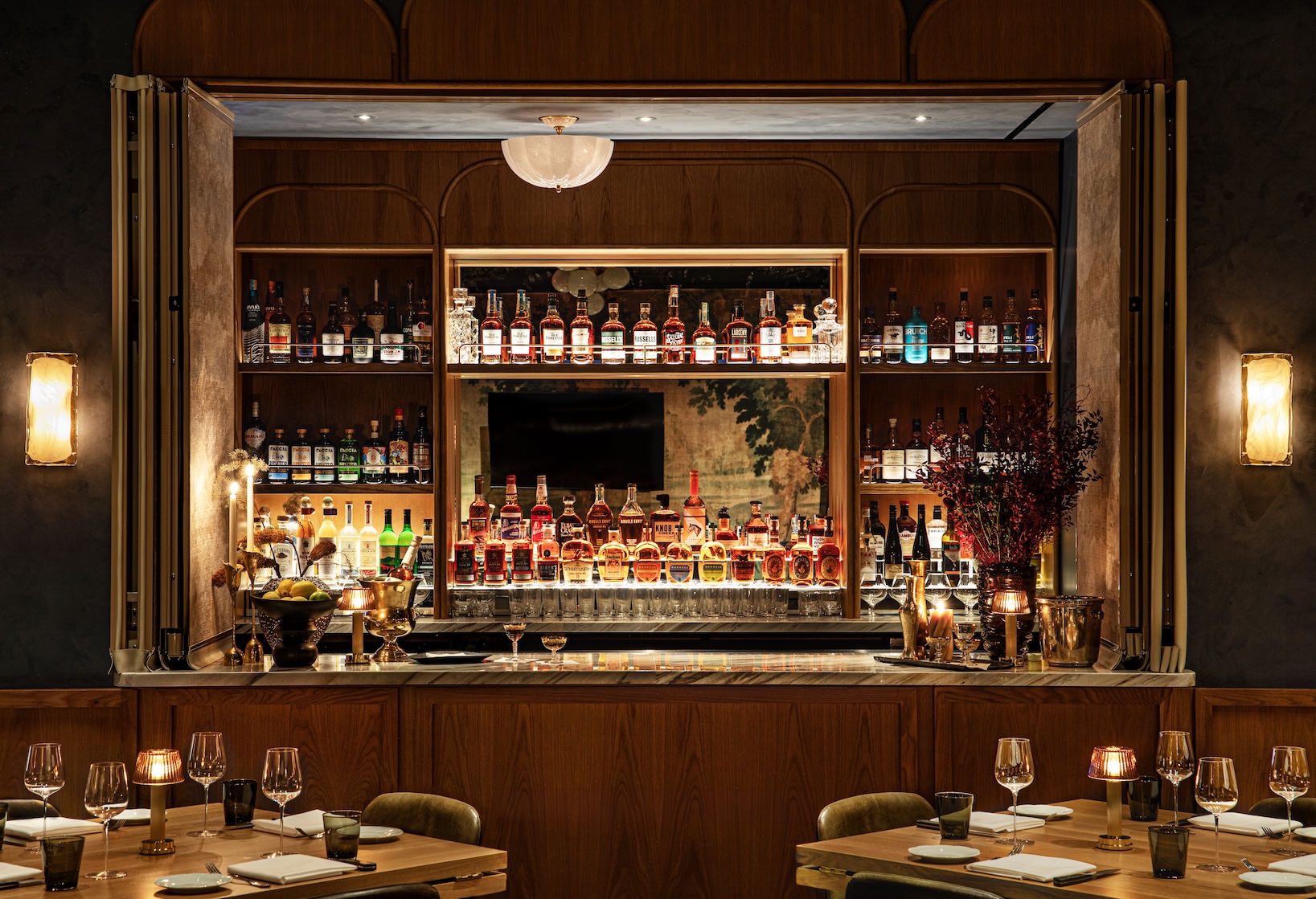 A speakeasy window filled with a view of the bar wall behind a set of tables, fully set for a meal