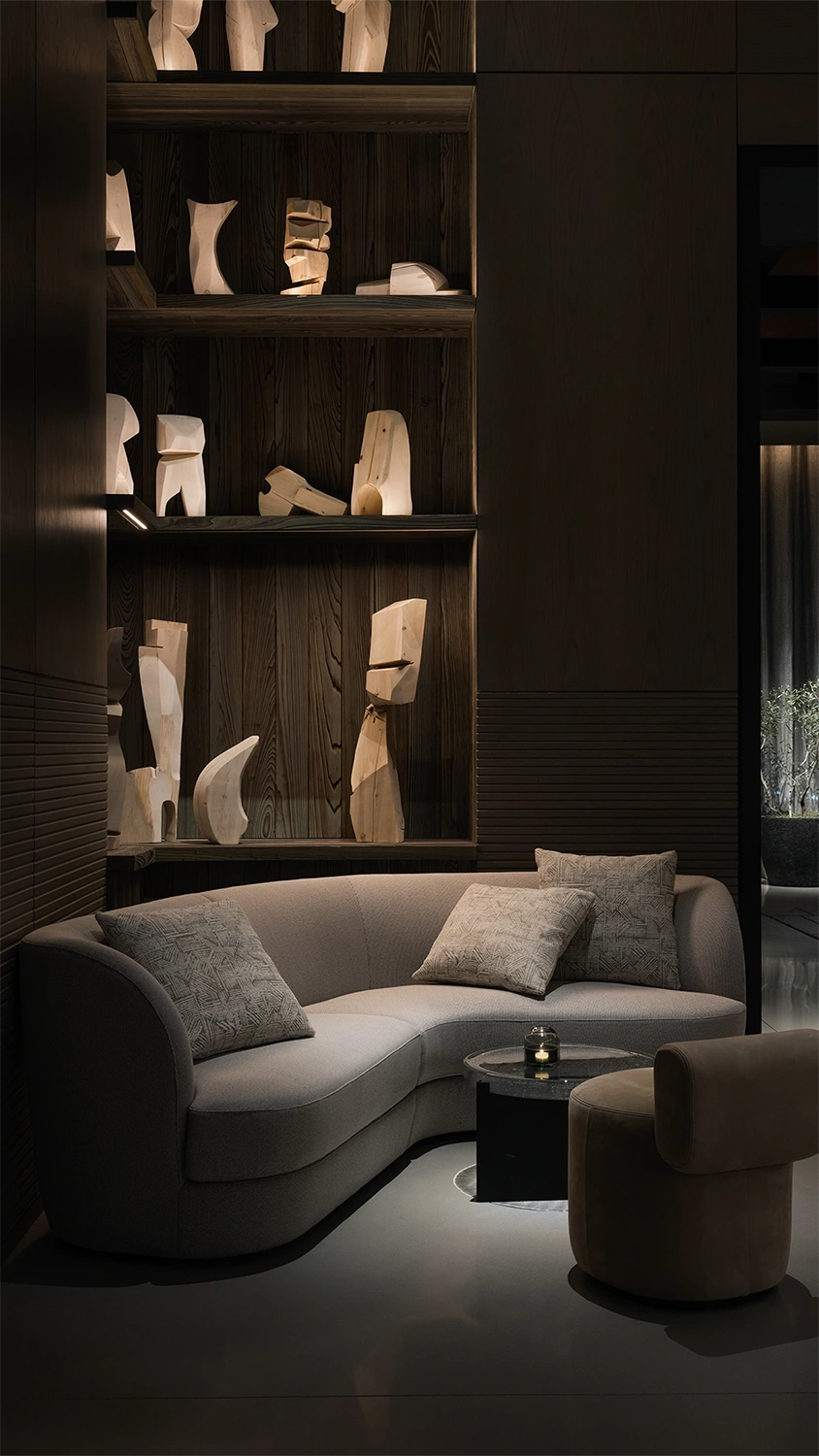 A moody hotel lounge area with a plush grey couch behind a small drinks table with a single candle lit.