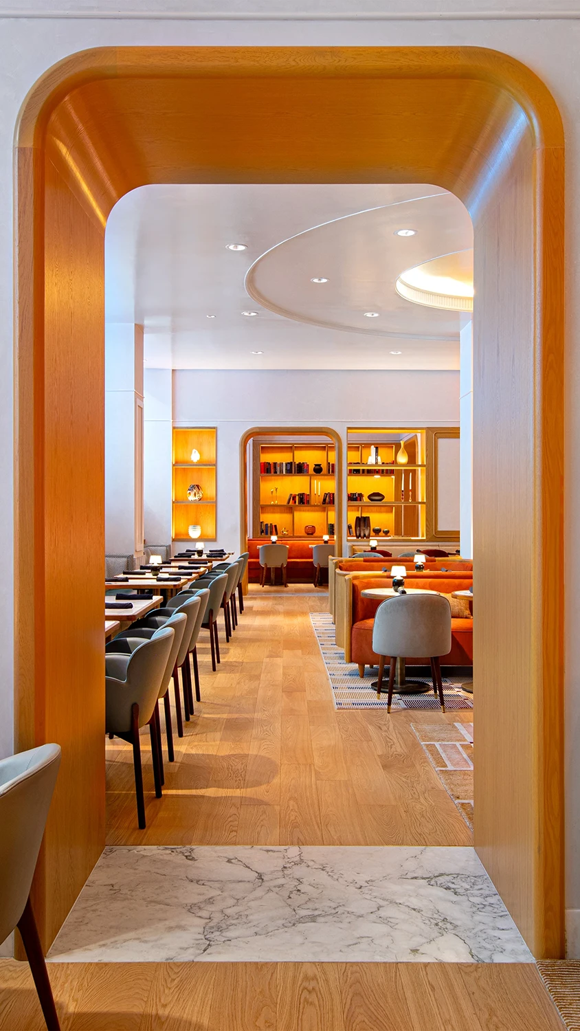 An arched golden doorway looking into a room lined with restaurant tables and lounge style seating.