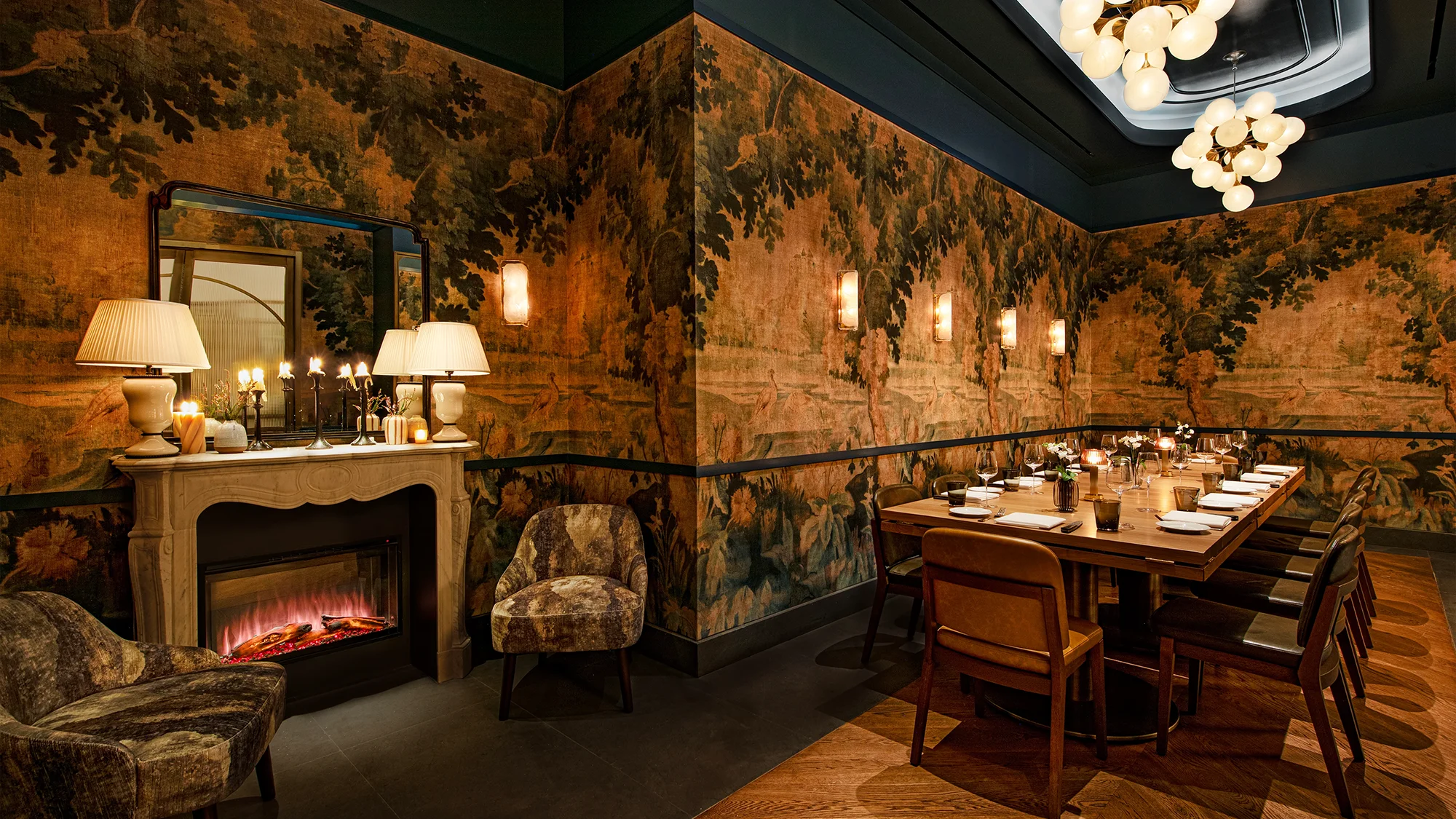 A restaurant private area seating featuring a long table set with plates, cutlery, and chairs, being lit by a cozy fireplace and unique lighting fixture