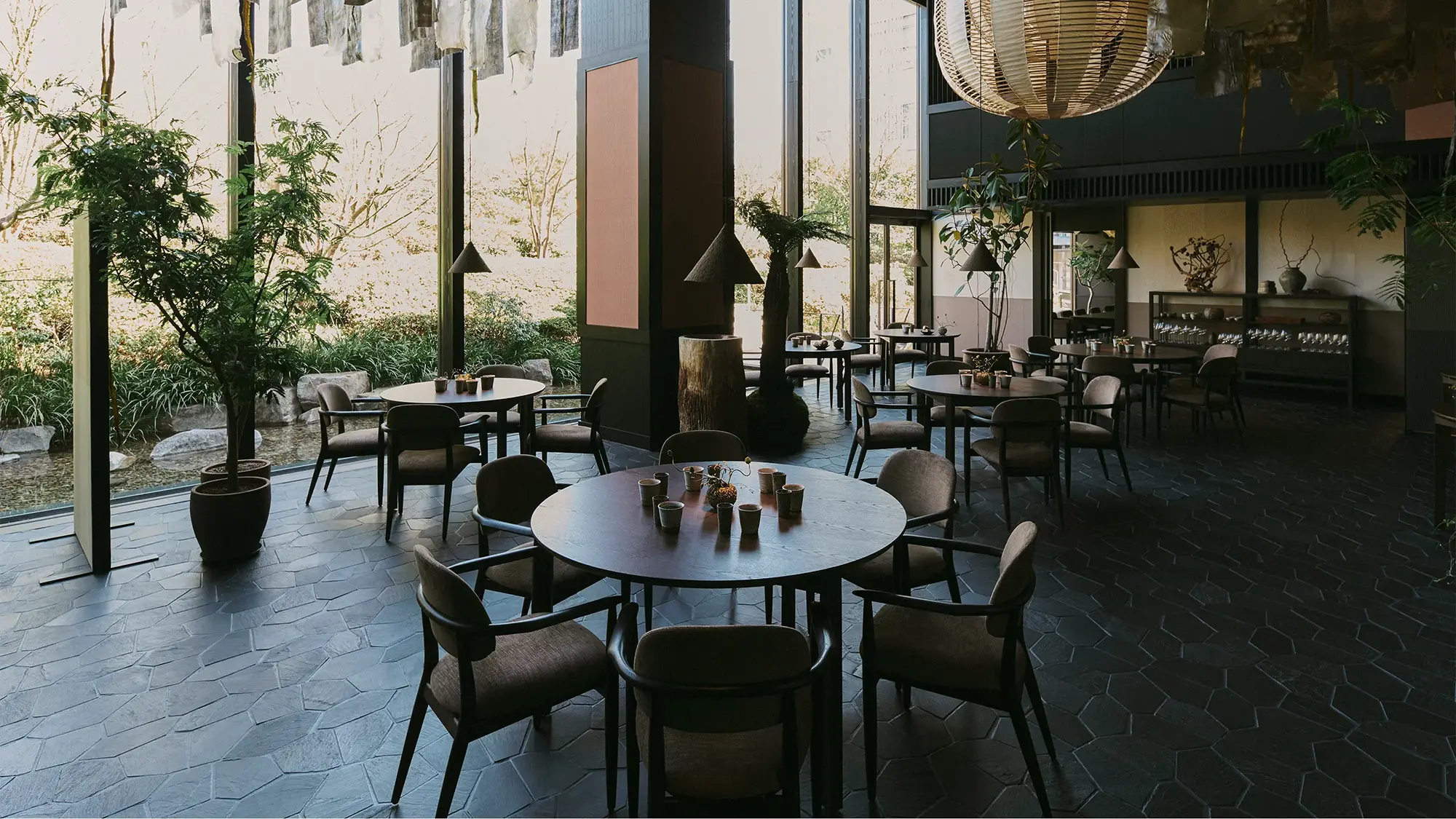 A contemporary oriental-Japanese designed restaurant dining room with circular wooden tables circled by upholstered chairs